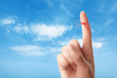 Image of Woman showing index finger with tied red bow as reminder against blue sky, closeup
