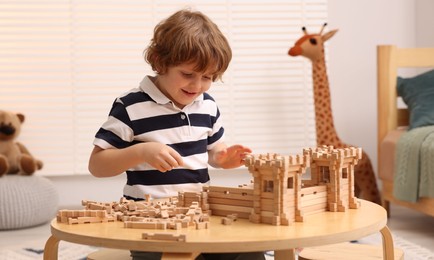 Photo of Little boy playing with wooden entry gate at table in room. Child's toy