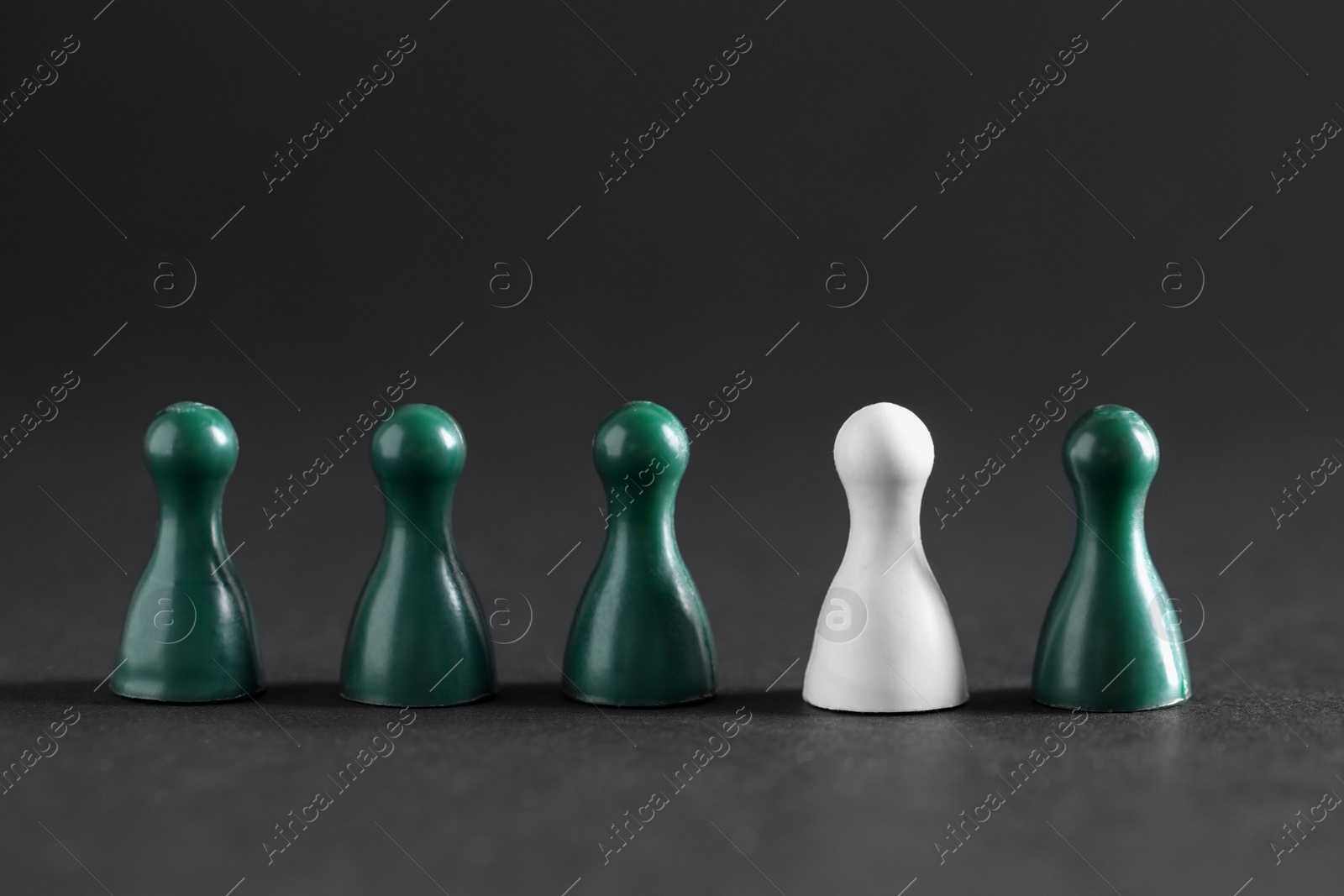 Photo of Choice concept. White pawn among green ones on dark table, closeup