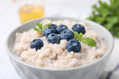 Photo of Delicious barley porridge with blueberries and mint in bowl on white table, closeup