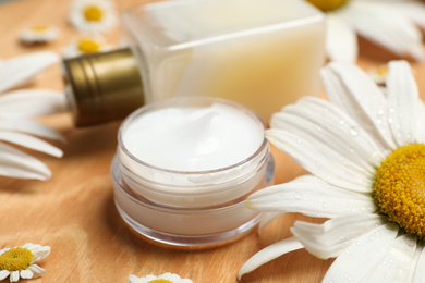 Composition with chamomile flowers and cosmetic products on wooden table, closeup