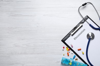 Clipboard with word Rheumatism, stethoscope and pills on white wooden table, flat lay. Space for text