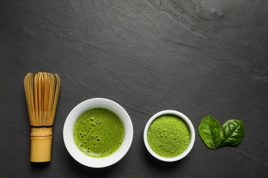 Photo of Cup of fresh matcha tea, green powder and bamboo whisk on black table, flat lay. Space for text