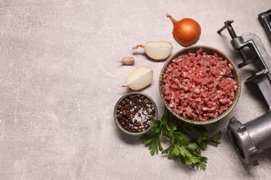 Manual meat grinder with beef mince, peppercorns, onion and parsley on light grey table, flat lay. Space for text