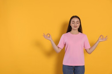 Find zen. Beautiful young woman meditating on yellow background. Space for text