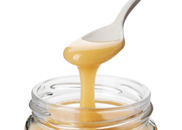 Photo of Honey dripping from spoon into jar on white background