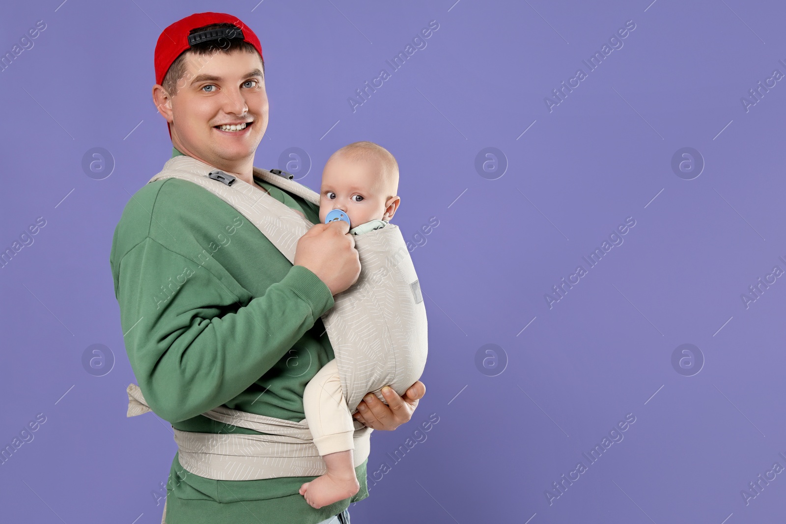 Photo of Father holding his child in sling (baby carrier) on purple background. Space for text