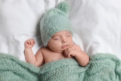 Photo of Cute little baby sleeping under knitted plaid in bed, top view