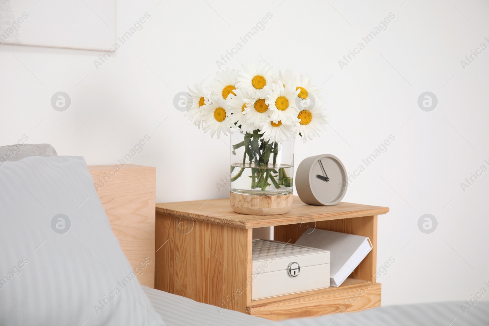 Photo of Bouquet of beautiful daisy flowers on wooden nightstand in bedroom