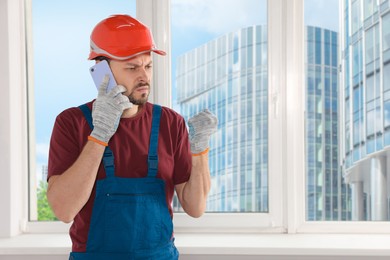 Professional repairman in uniform talking on phone indoors, space for text