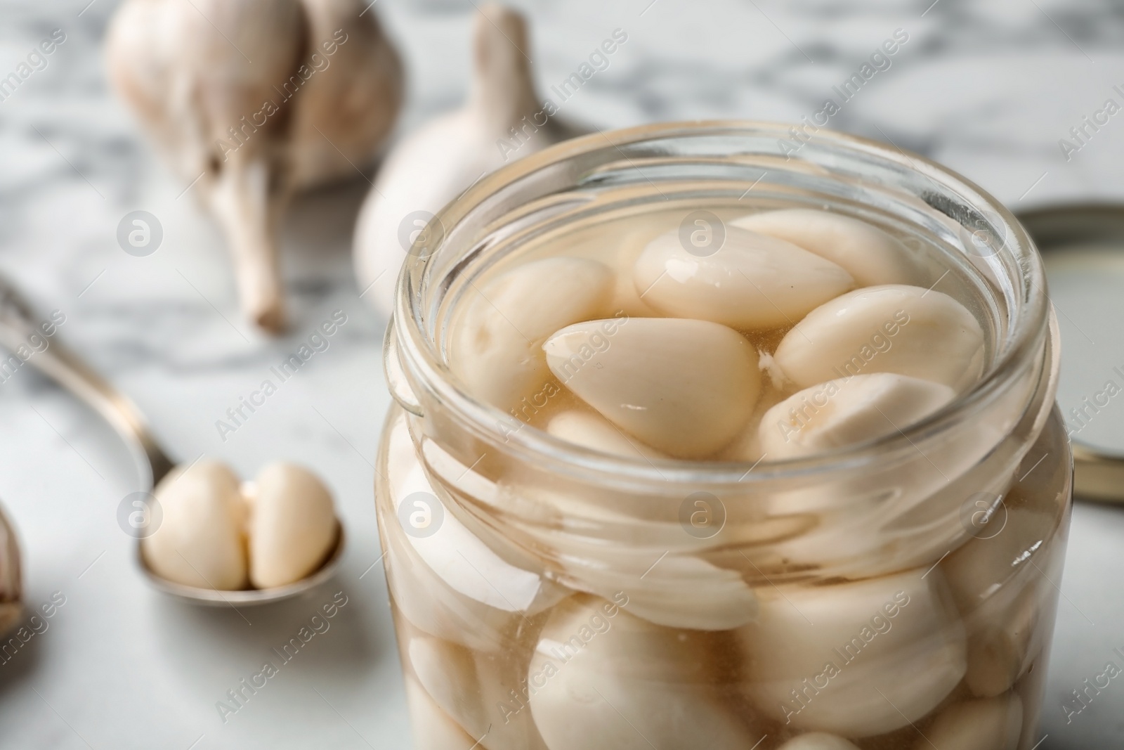 Photo of Preserved garlic in glass jar on table, closeup. Space for text