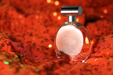 Photo of Luxury perfume in bottle on red fabric with sequins, closeup