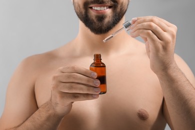 Man with cosmetic serum in hands on light grey background, closeup