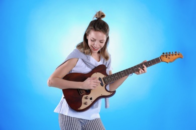 Young woman playing electric guitar on color background