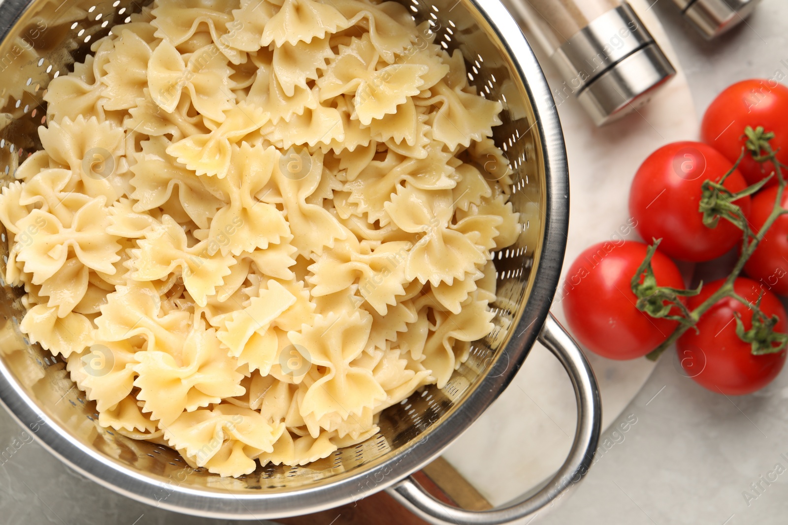 Photo of Cooked pasta in metal colander, spices and tomatoes on grey table, flat lay