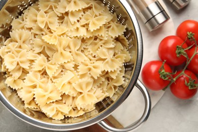 Cooked pasta in metal colander, spices and tomatoes on grey table, flat lay