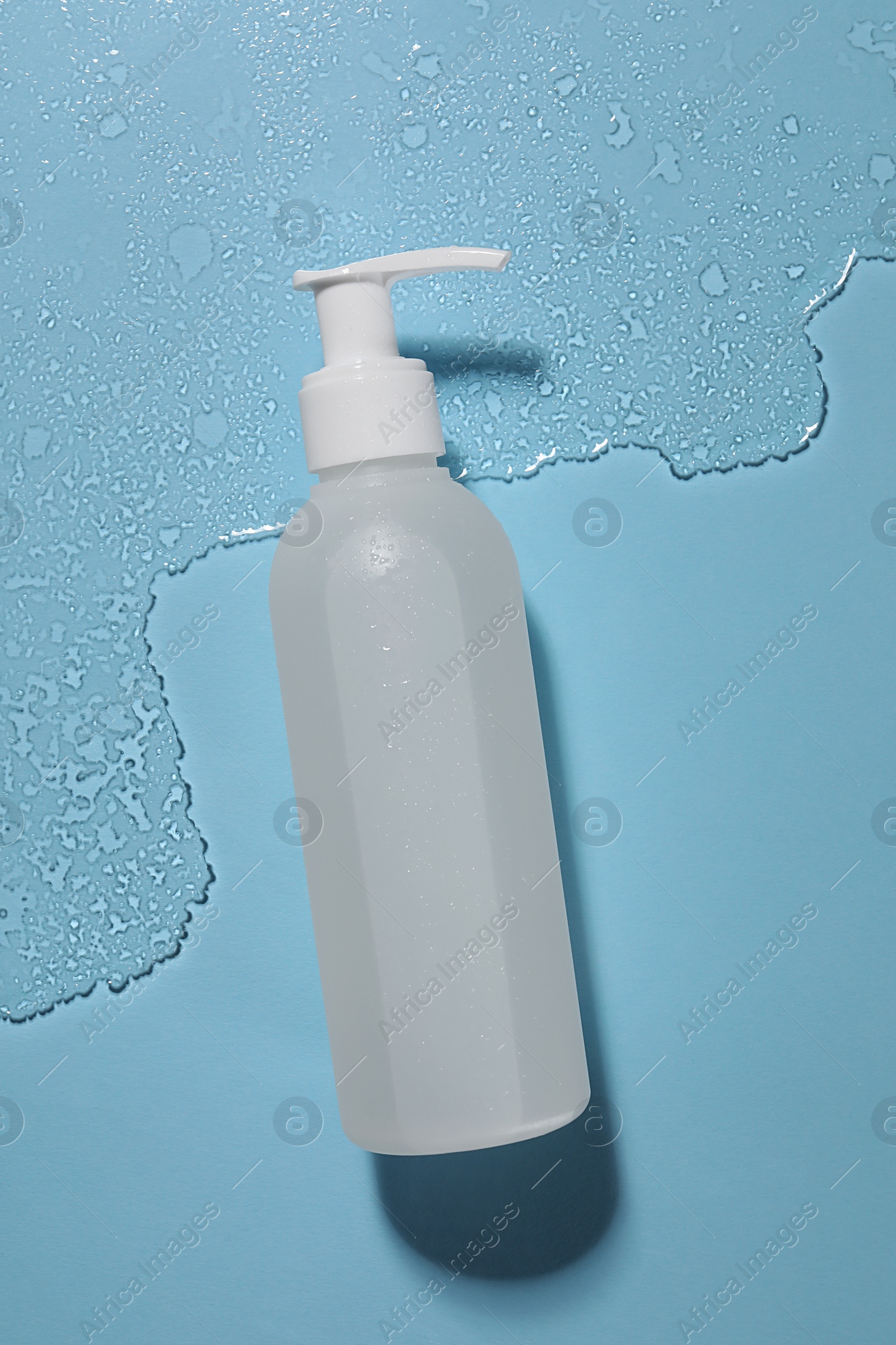 Photo of Bottle of face cleansing product in water against light blue background, top view