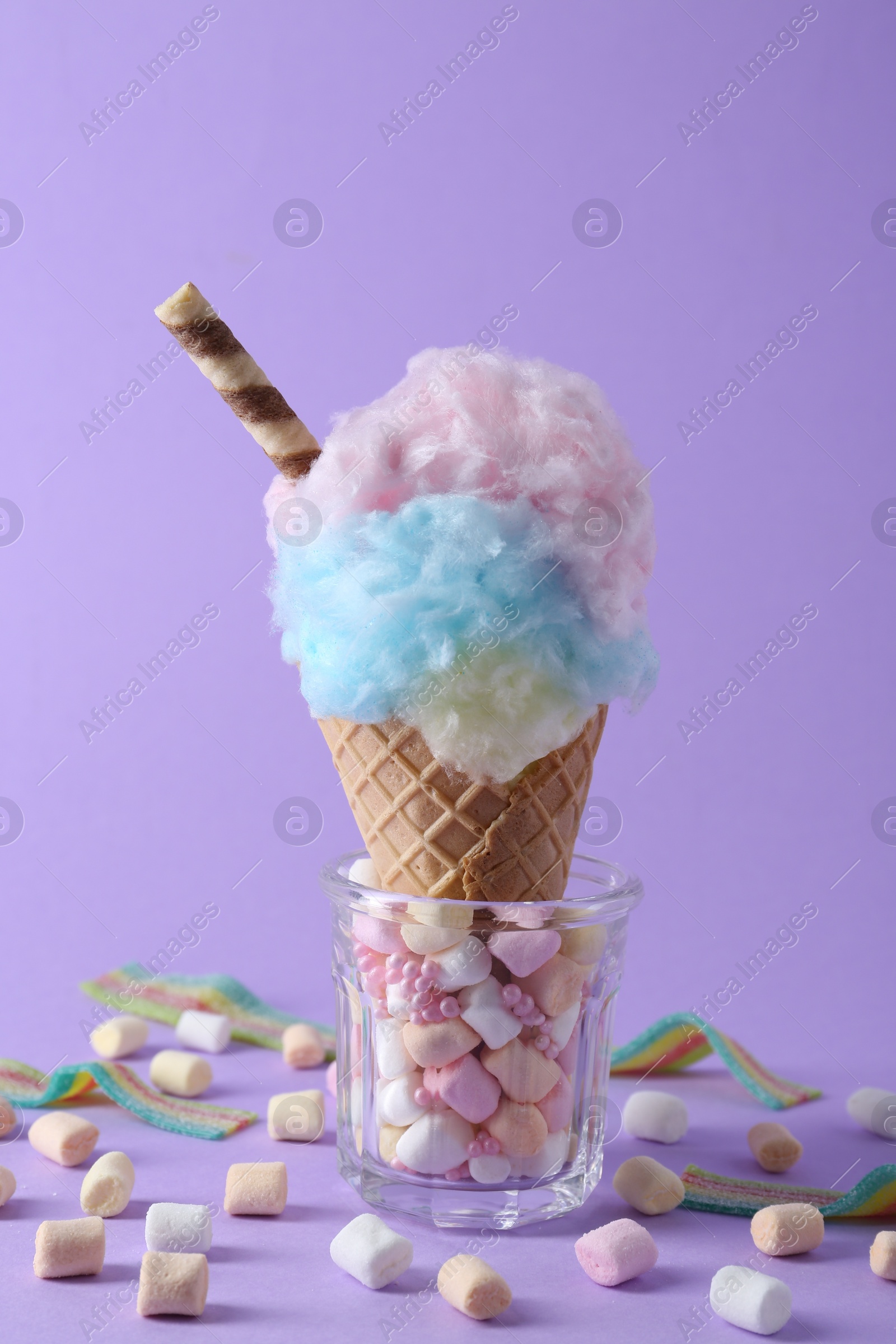 Photo of Sweet cotton candy in waffle cone and marshmallows on purple background