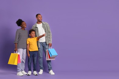 Photo of Family shopping. Happy parents and son with colorful bags on violet background, space for text