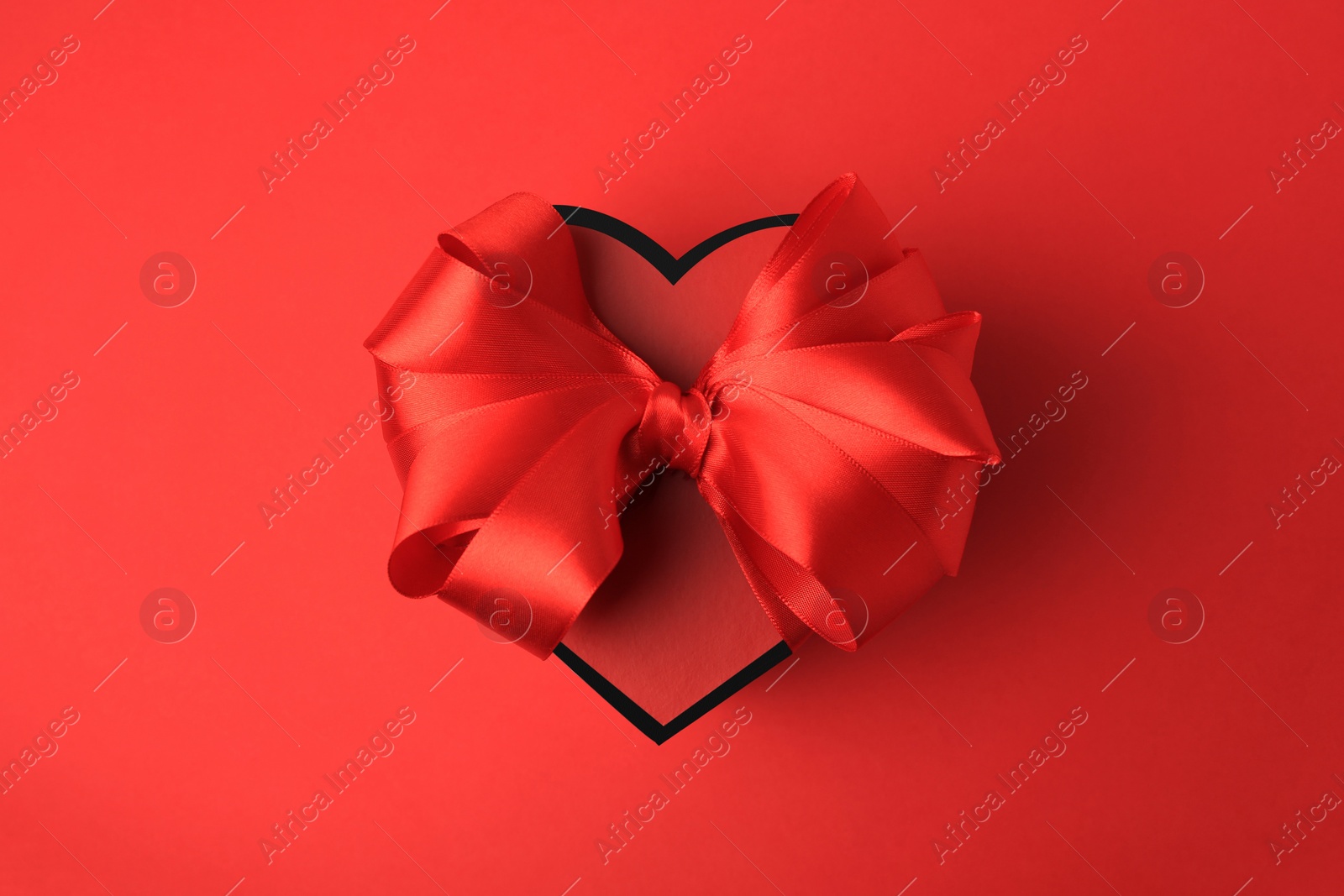 Photo of Beautiful heart shaped gift box with bow on red background, top view