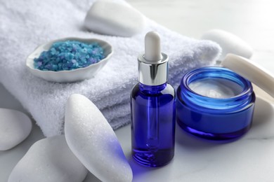 Photo of Spa composition. Cosmetic products, sea salt, towel and stones on white table, closeup