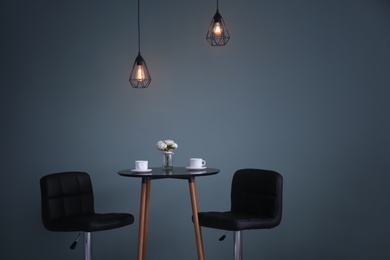Photo of Table with chairs against dark wall. Elegant interior