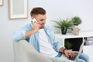 Photo of Young man talking on phone while using laptop at home