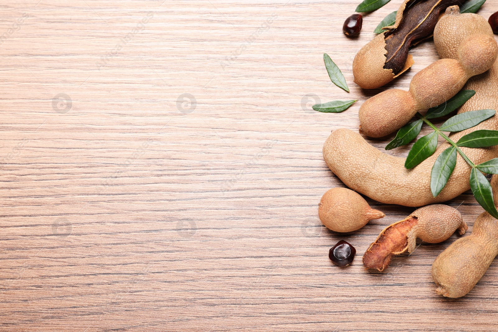 Photo of Delicious ripe tamarinds and leaves on wooden table, flat lay. Space for text