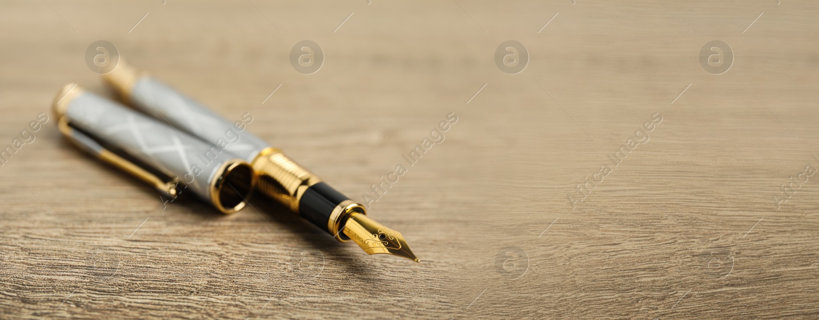 Image of Beautiful fountain pen with ornate nib on wooden table, closeup view with space for text. Banner design