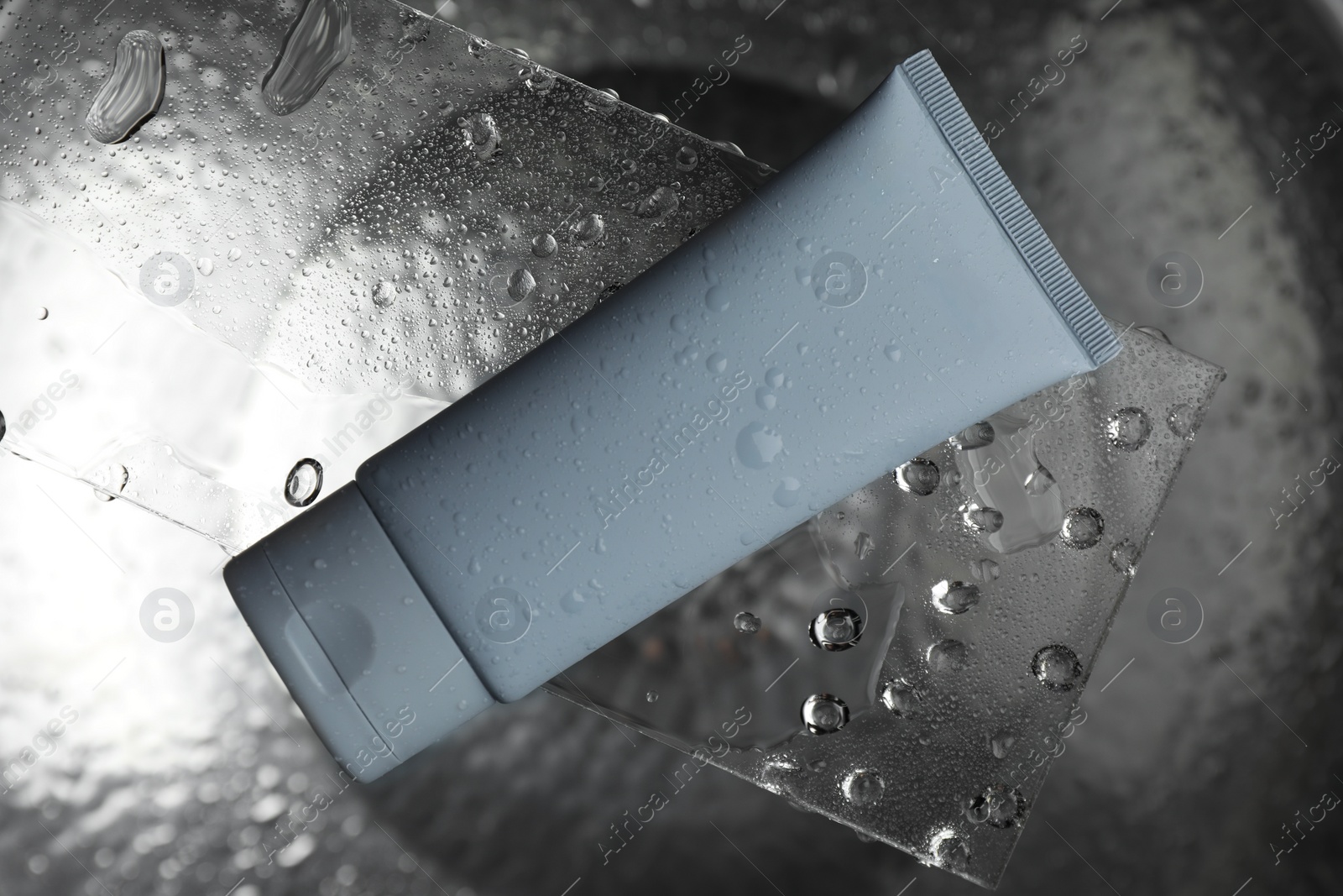 Photo of Moisturizing cream in tube on glass with water drops against metal background, top view