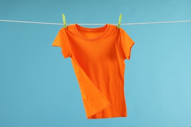 One orange t-shirt drying on washing line against light blue background