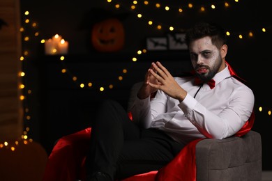 Photo of Man in scary vampire costume against blurred lights indoors, space for text. Halloween celebration