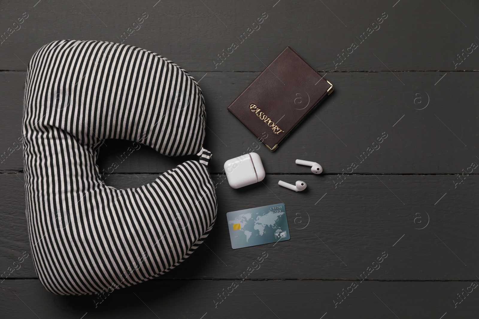 Photo of Striped travel pillow, passport, credit card and earphones on black wooden background, flat lay. Space for text