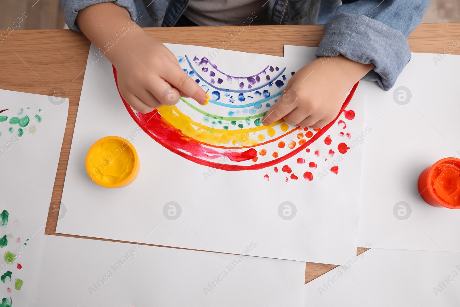 Photo of Little child painting with finger at wooden table indoors, top view