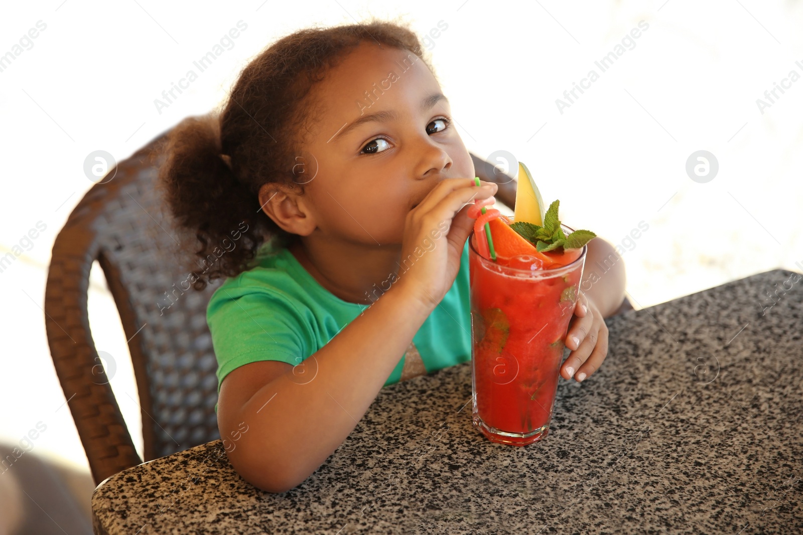 Photo of Cute African-American girl with glass of natural lemonade at table in cafe