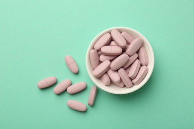 Pink vitamin capsules and bowl on turquoise background, top view