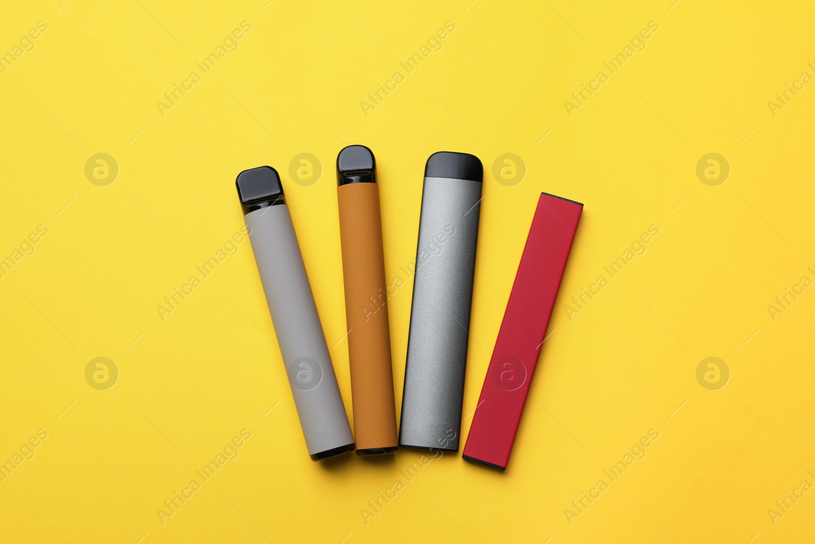 Photo of Different electronic cigarettes on yellow background, flat lay