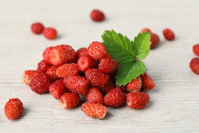 Photo of Pile of wild strawberries and leaves on white wooden table, closeup