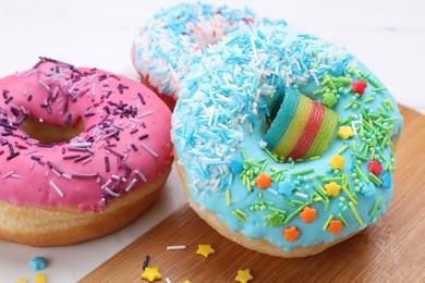 Photo of Sweet glazed donuts decorated with sprinkles on board, closeup. Tasty confectionery