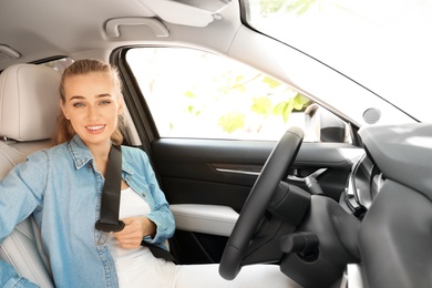 Photo of Female driver fastening safety belt in car