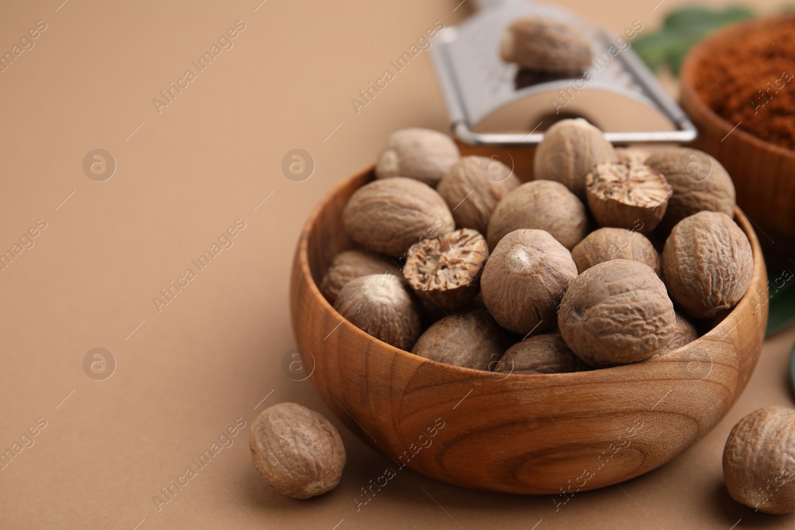 Photo of Nutmegs in bowl on light brown background, closeup. Space for text