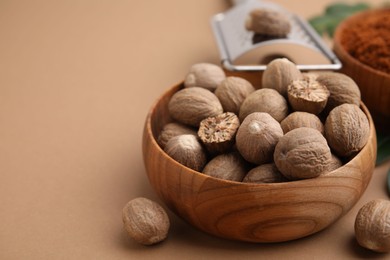 Photo of Nutmegs in bowl on light brown background, closeup. Space for text