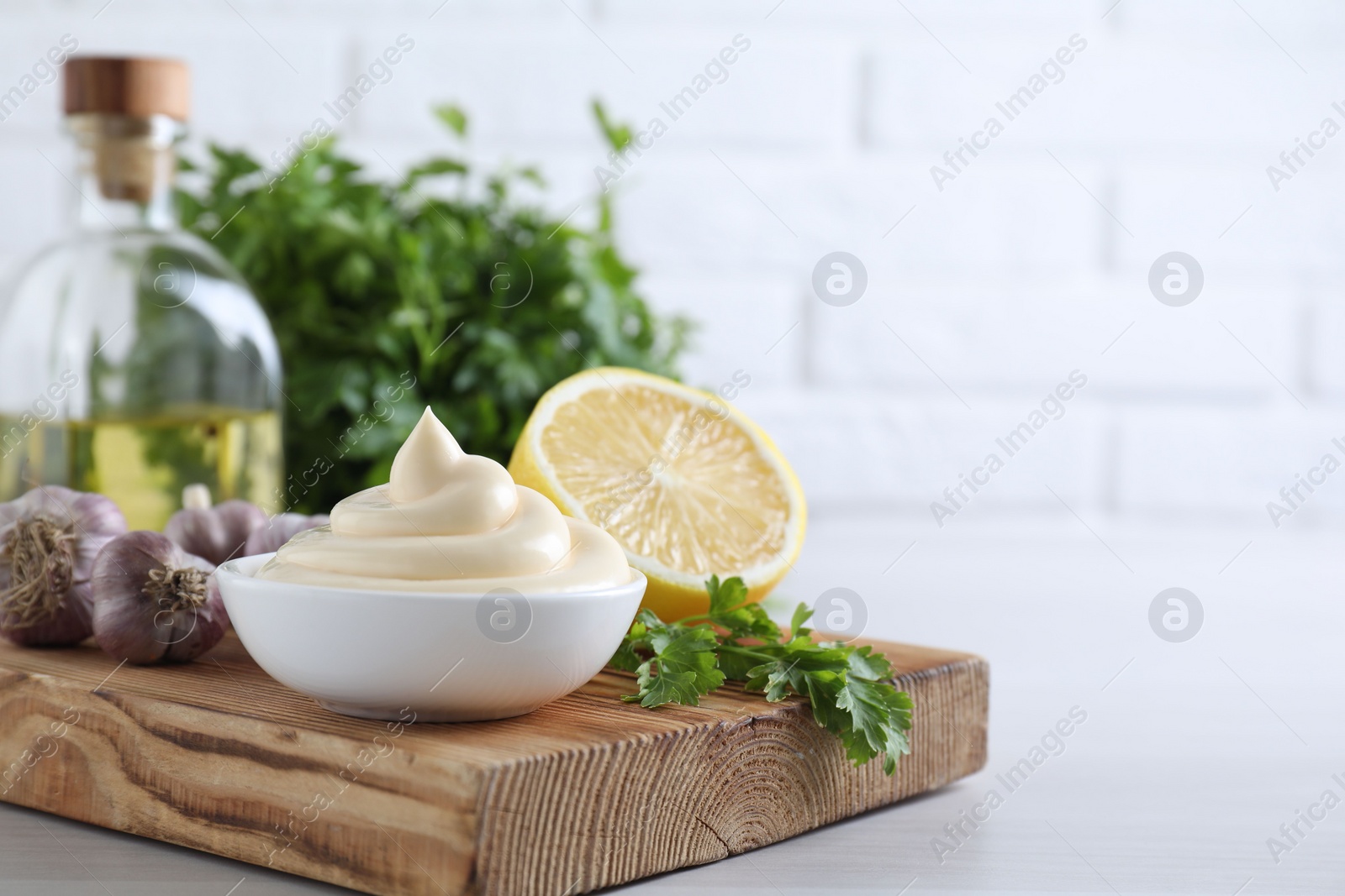 Photo of Tasty mayonnaise sauce in bowl, parsley, garlic and lemon on white wooden table, closeup. Space for text