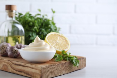 Tasty mayonnaise sauce in bowl, parsley, garlic and lemon on white wooden table, closeup. Space for text