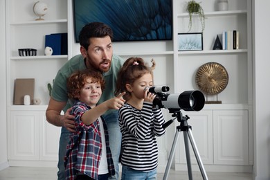 Happy father and children looking at stars through telescope in room