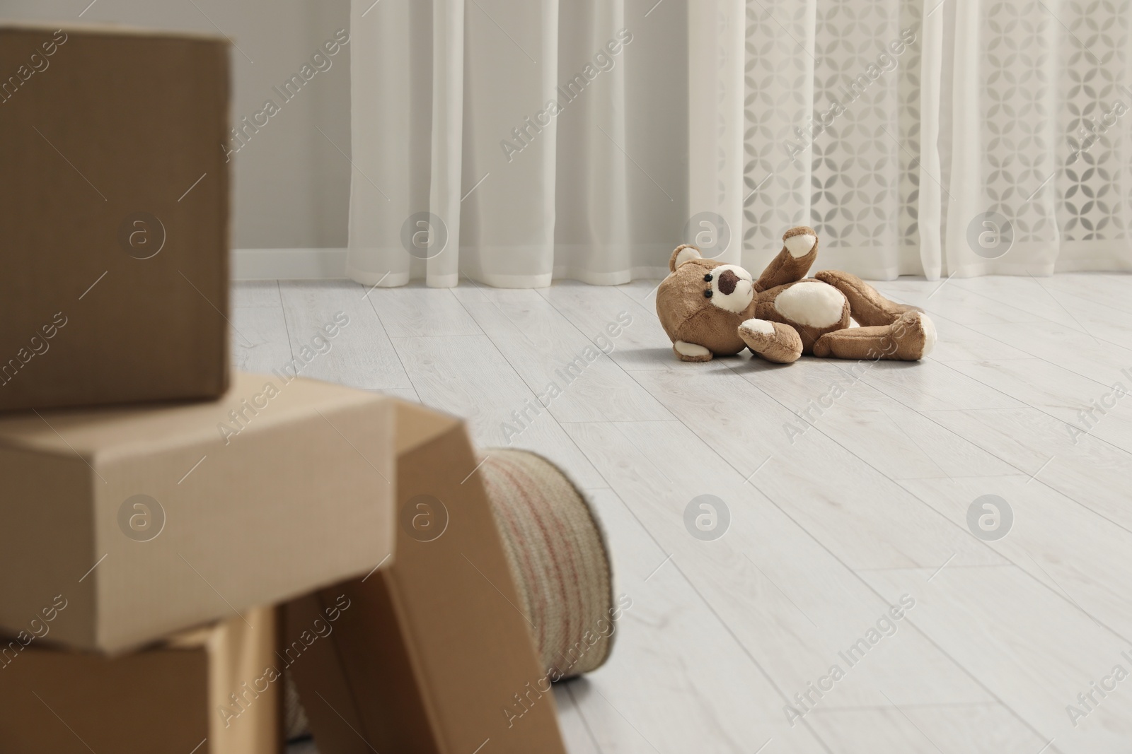 Photo of Cute lonely teddy bear on floor near boxes indoors