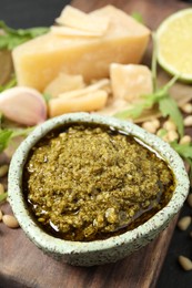 Photo of Bowl of tasty arugula pesto and ingredients on table, closeup