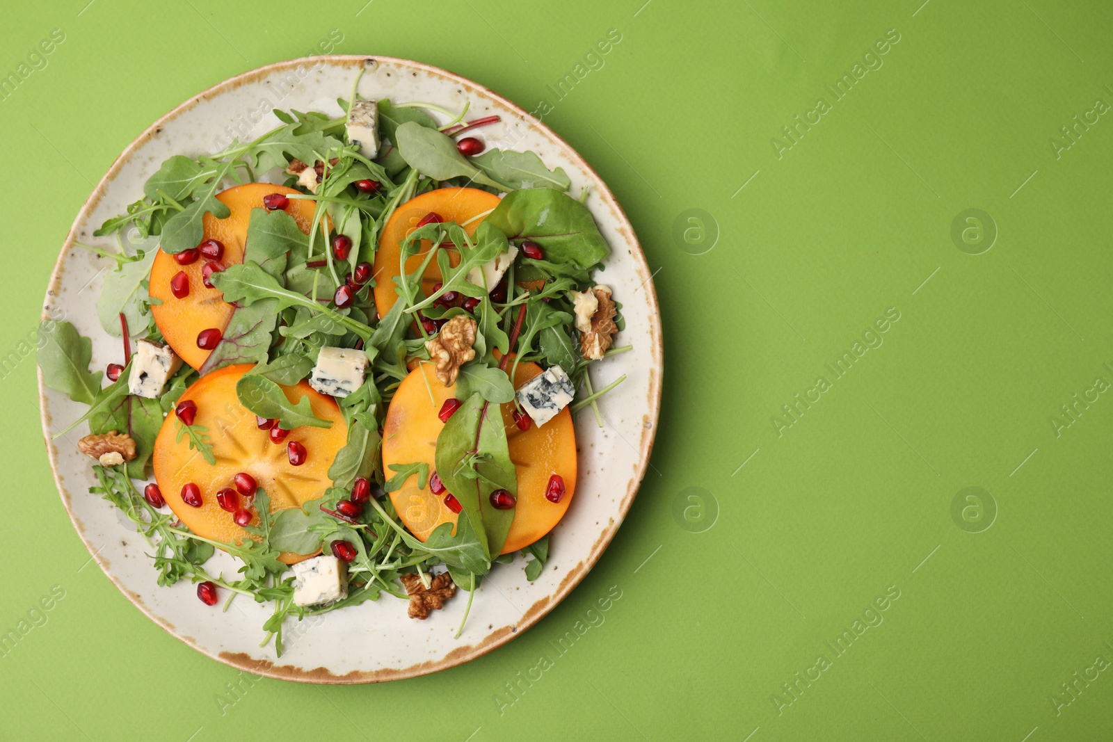 Photo of Tasty salad with persimmon, blue cheese and walnuts served on light green background, top view. Space for text