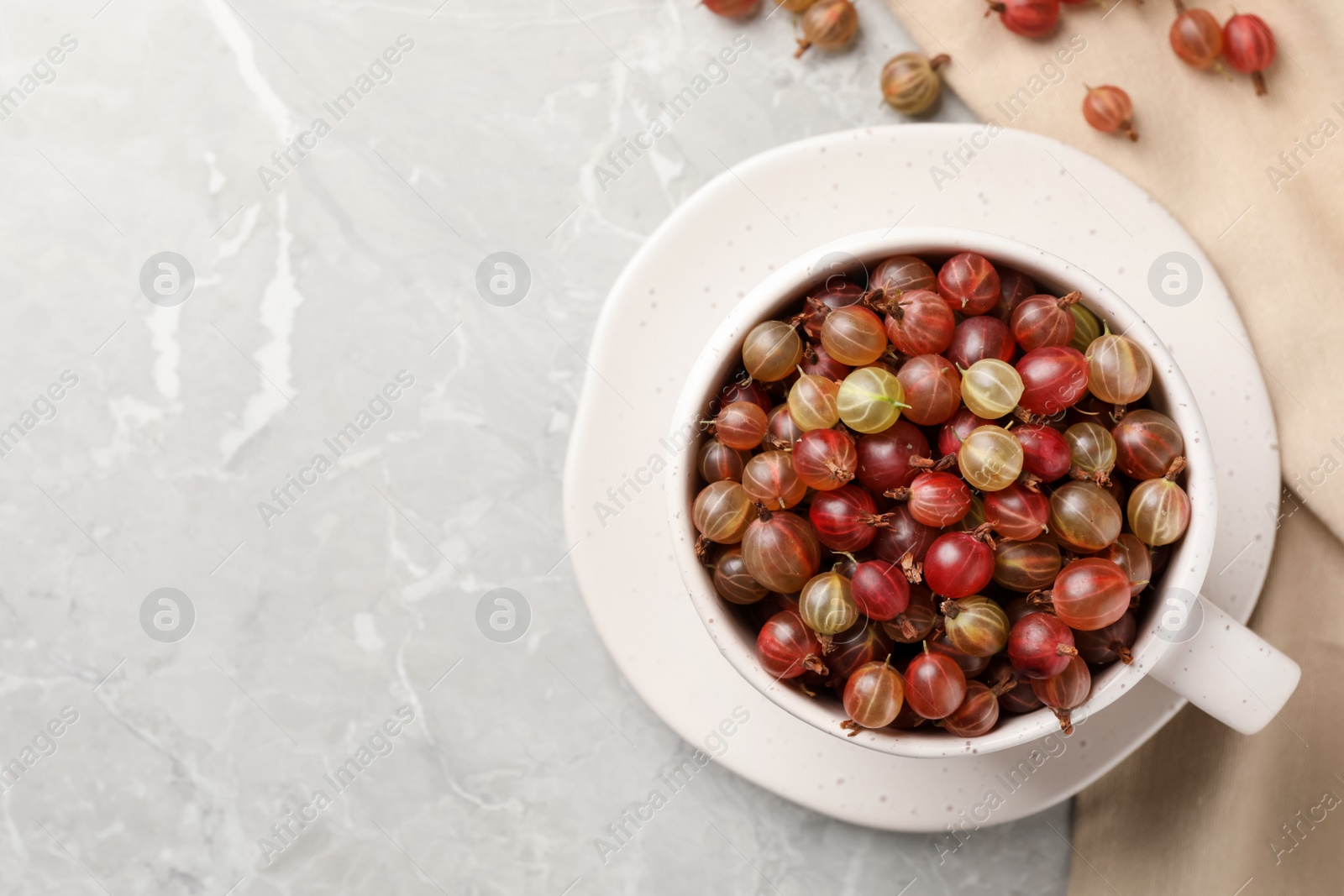 Photo of Cup with ripe gooseberries on light grey marble table, flat lay. Space for text