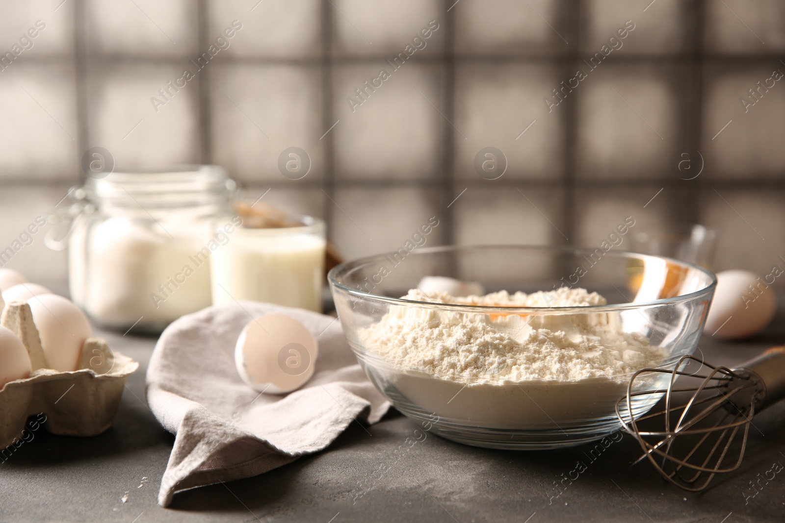 Photo of Making dough. Flour with in bowl and whisk on grey textured table, closeup